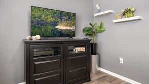 Ein Wohnzimmer mit Flachbildfernseher, dunklem Holzschrank und dekorativen Regalen.