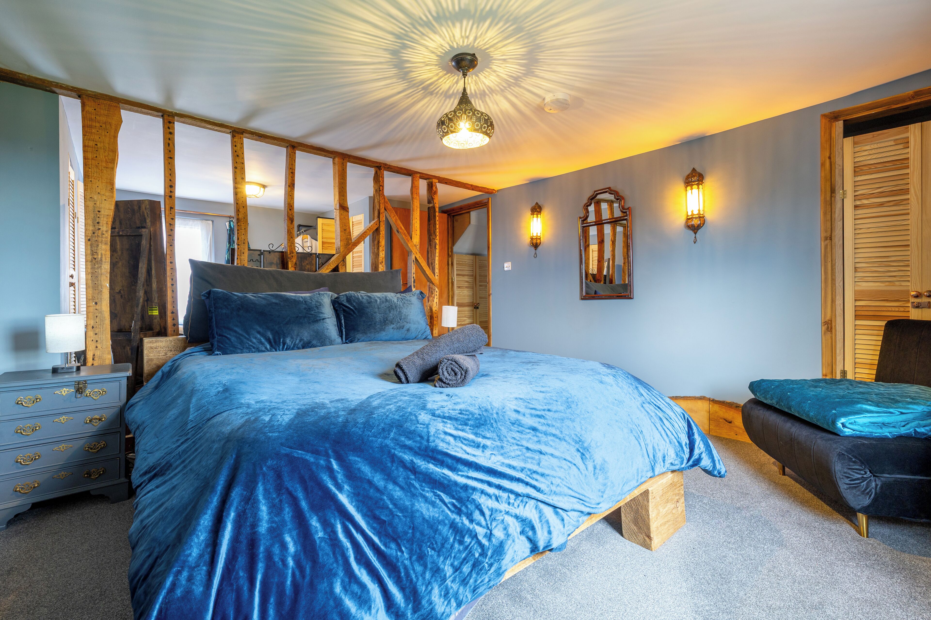 A bedroom with a large bed, wooden beams, a bench, and a small table.