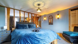 Une chambre avec un grand lit, des poutres en bois, un banc et une petite table.