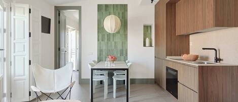 A modern kitchen with wooden cabinets, a built-in oven, and a sink. There is a dining area with a table and chairs, and a small round table with a book.