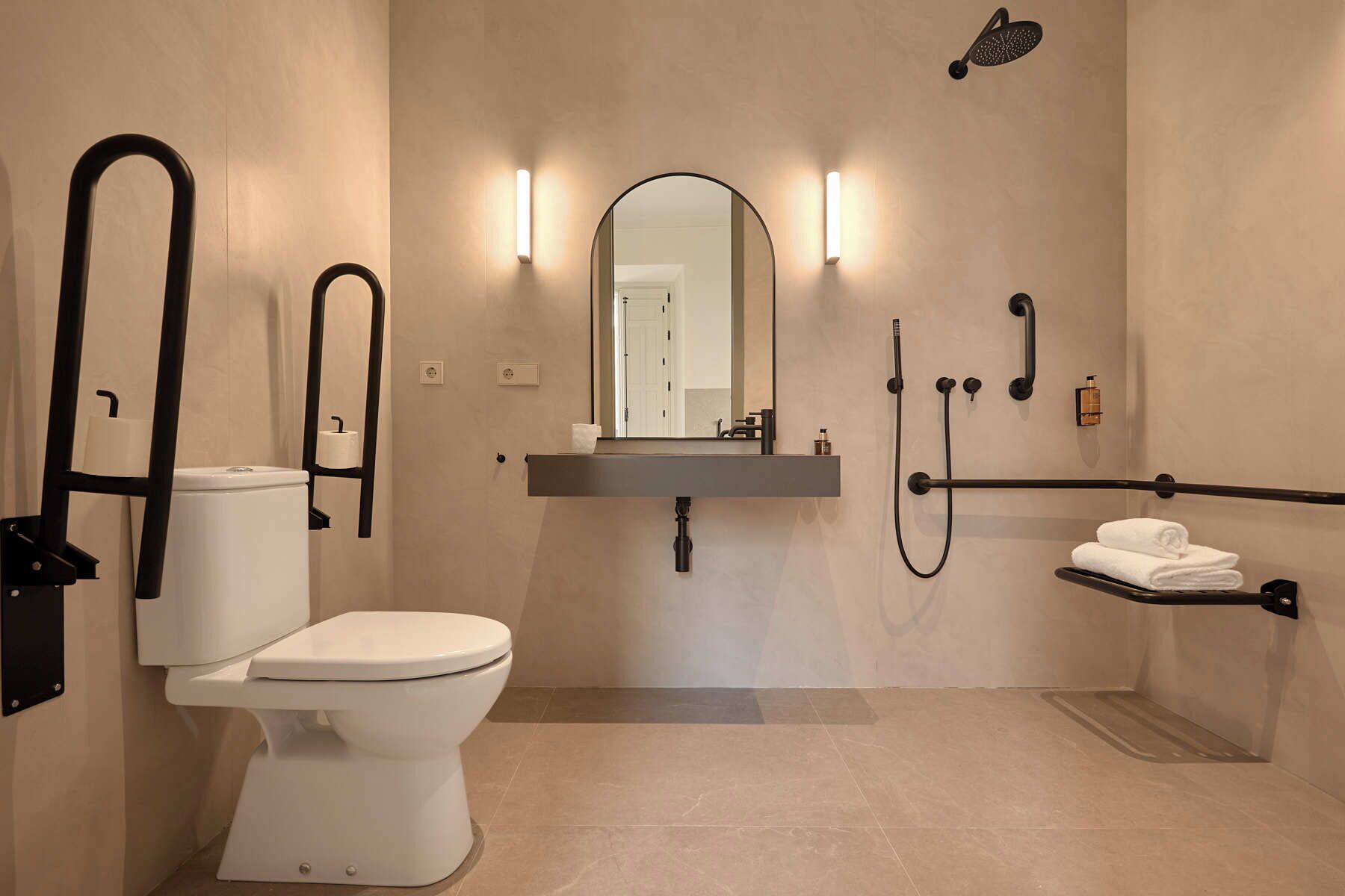 A modern bathroom with a toilet, sink, mirror, shower, and towel rack.