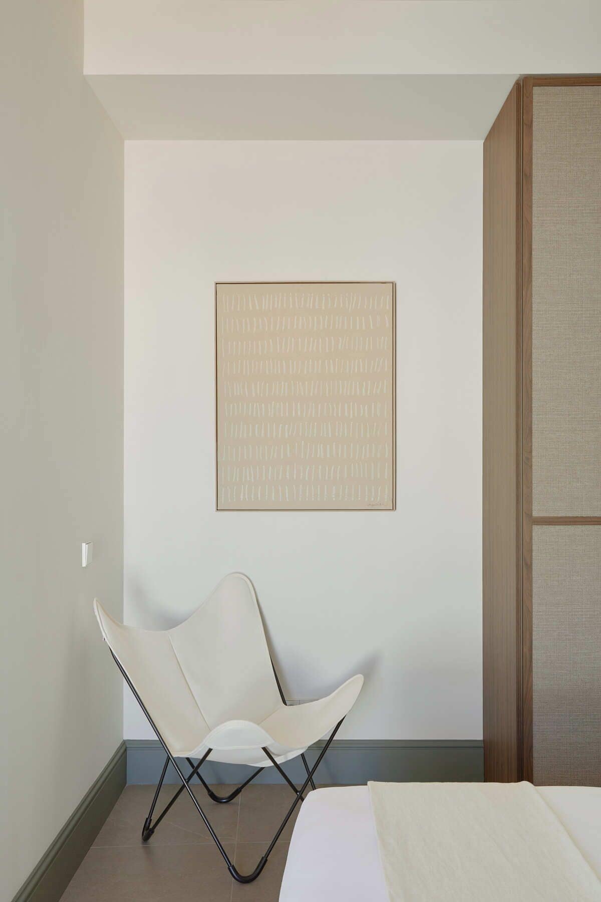 Una habitación de hotel moderna con diseño minimalista, que presenta una silla blanca, una obra de arte grande con marco y un armario de madera.