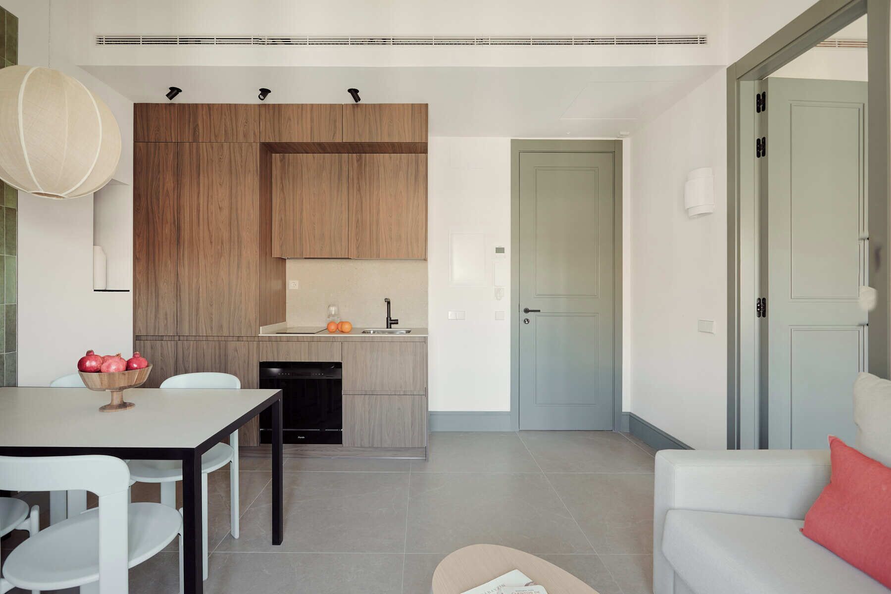 A modern kitchen with wooden cabinets, a dining table with chairs, and a small island with a bowl of fruit.