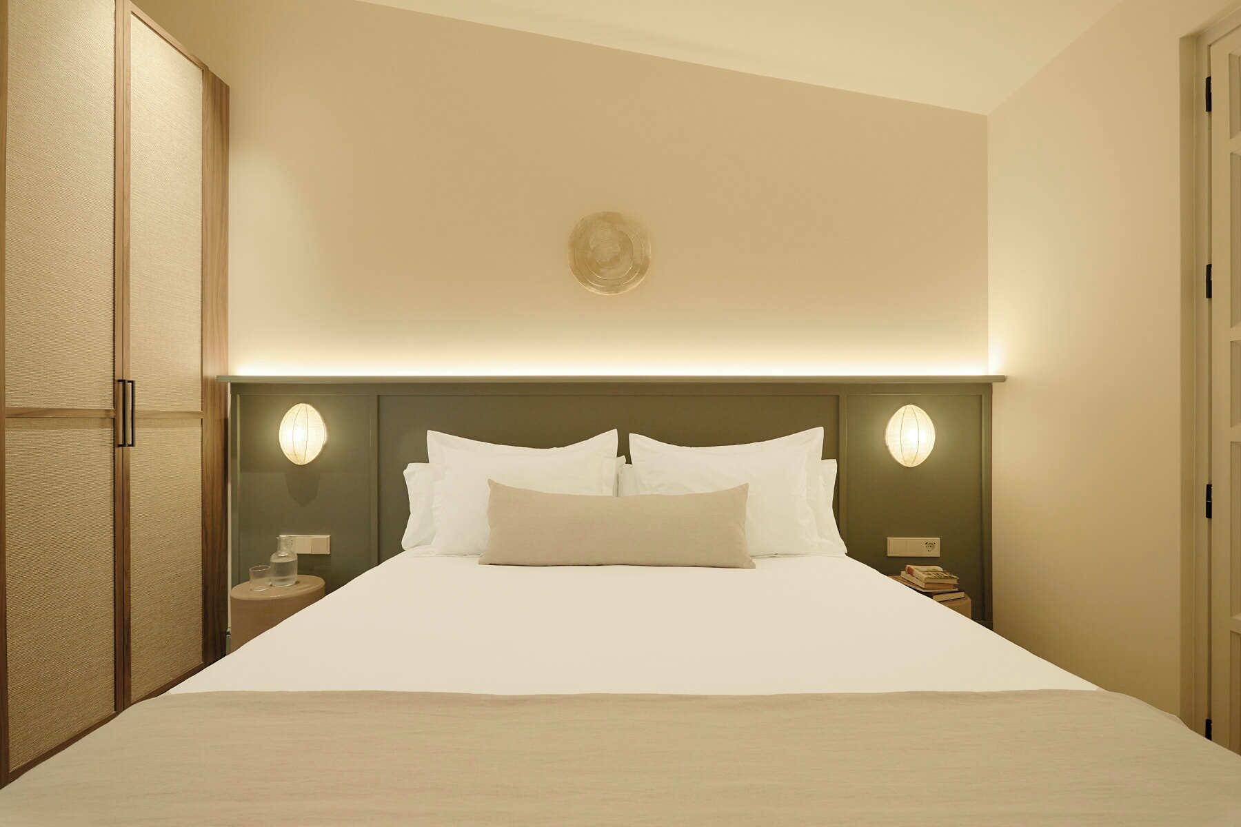 Habitación de hotel con una cama grande, dos mesitas de noche y cabecera con iluminación integrada.
