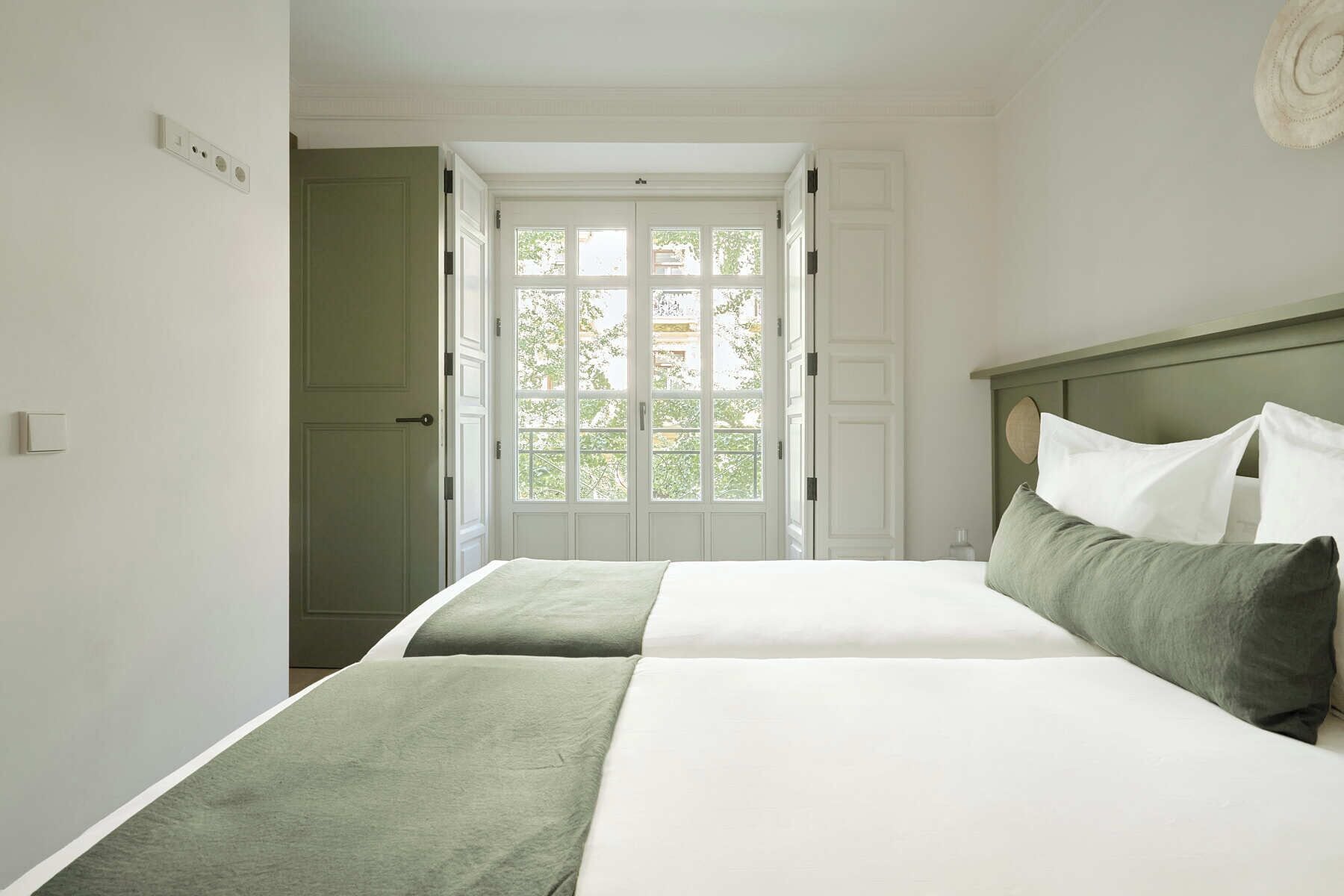 A bedroom with a bed, a nightstand, and a window with a view of greenery.