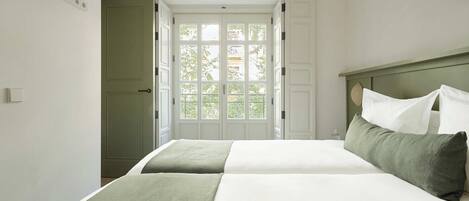 A bedroom with a bed, a nightstand, and a window with a view of greenery.