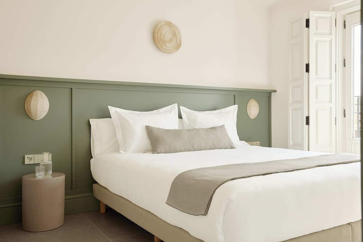 A neatly made bed with a green headboard, a bedside table with glasses, and a round wall decoration.