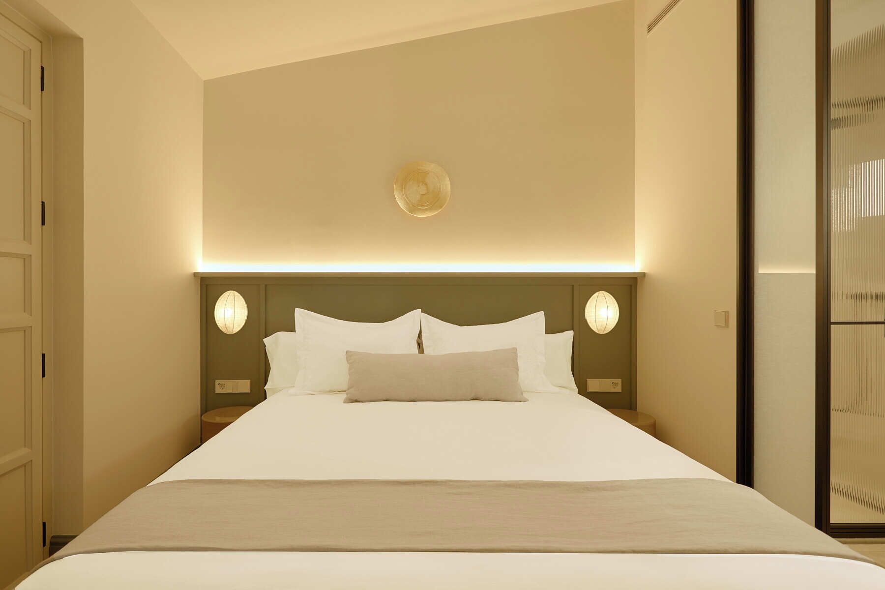 Een hotelkamer met een groot bed, een hoofdeinde met ingebouwde verlichting en uitzicht op een schuifdeur.