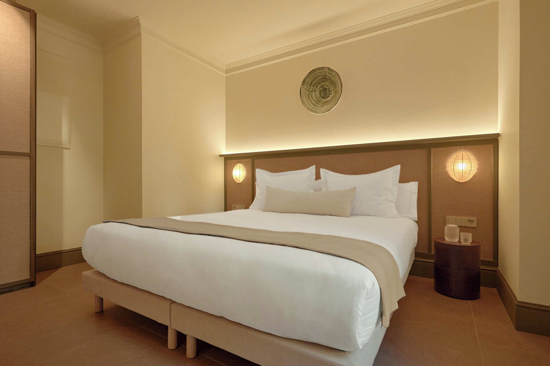 A large bed with a headboard, two bedside lamps, and a small table with a lamp.