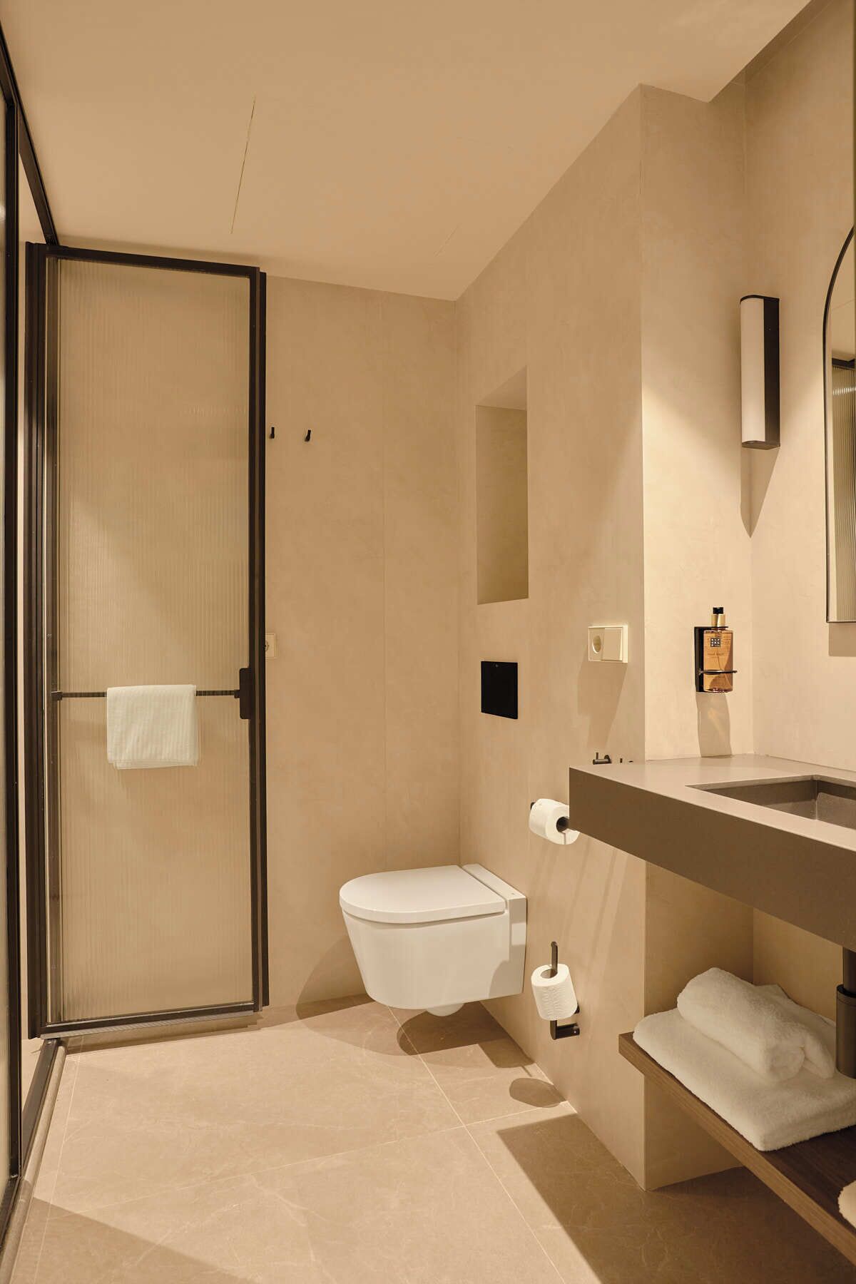A modern bathroom with a walk-in shower, toilet, and vanity with a mirror and towel rack.