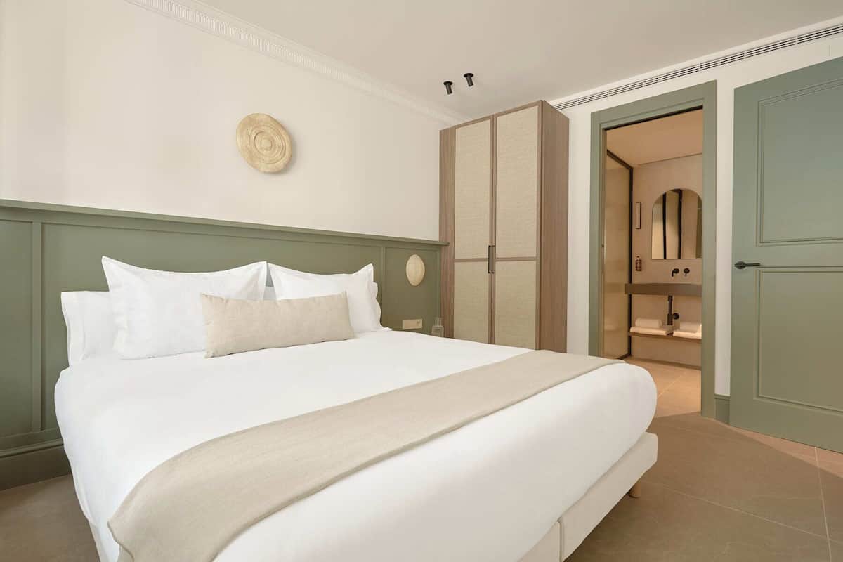 A neatly made bed with white linens and a beige throw blanket in a room with a green headboard.