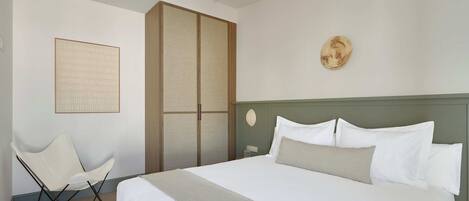 Habitación de hotel ordenada con una cama grande, una silla, un armario y una obra de arte colgada en la pared.