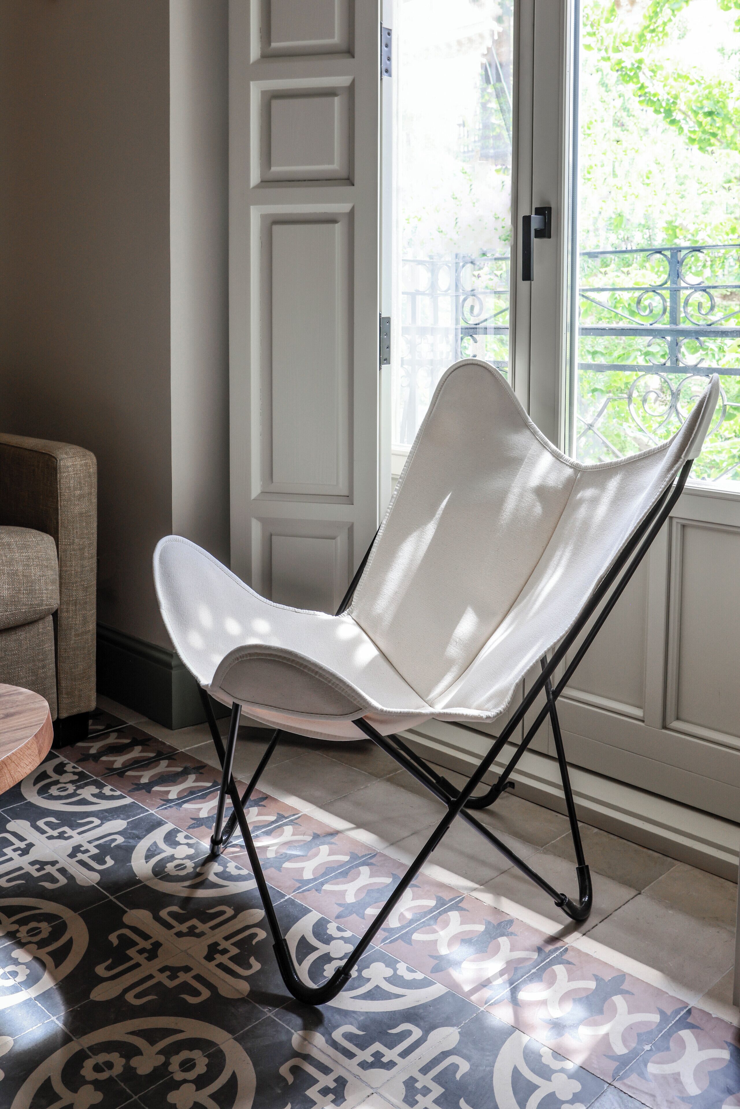 A white chair with a unique design, positioned near a door with a view of greenery outside.