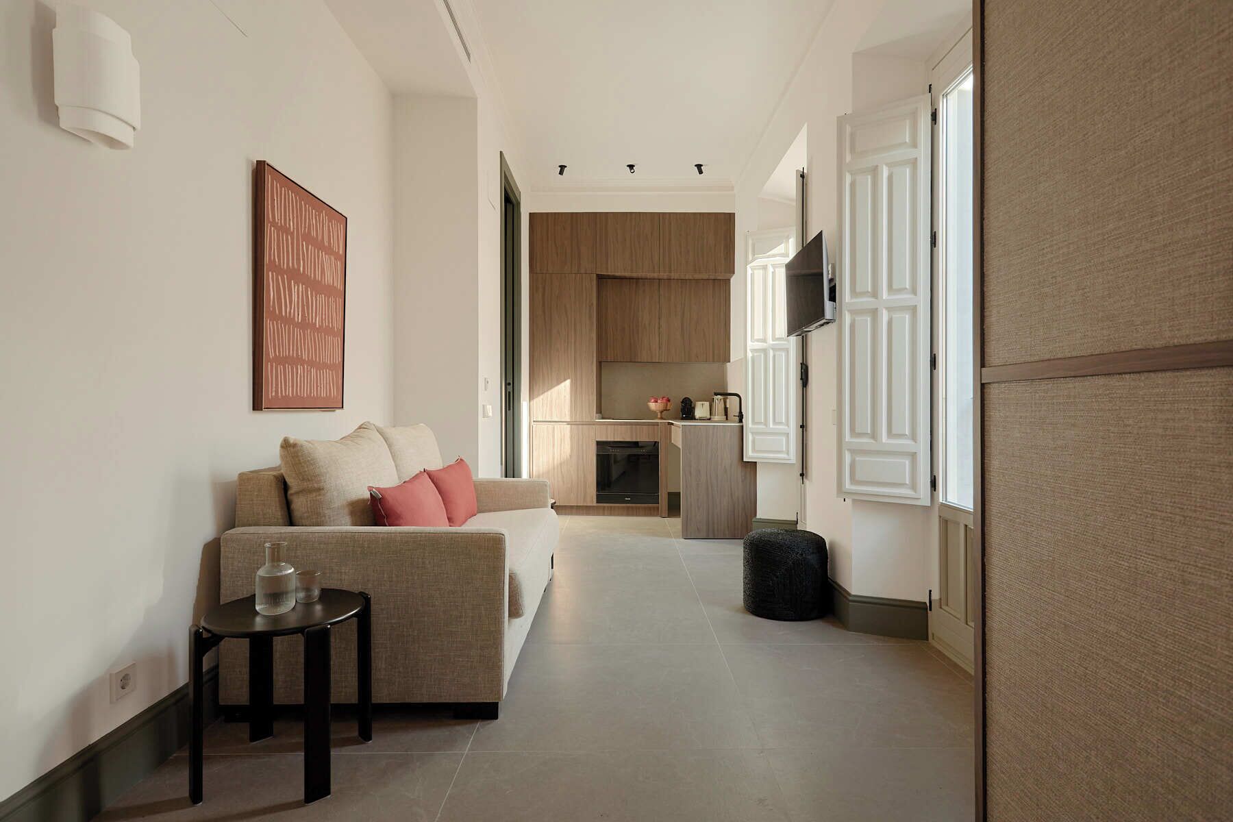 A modern living room with a sofa, a small table, and a kitchen in the background.