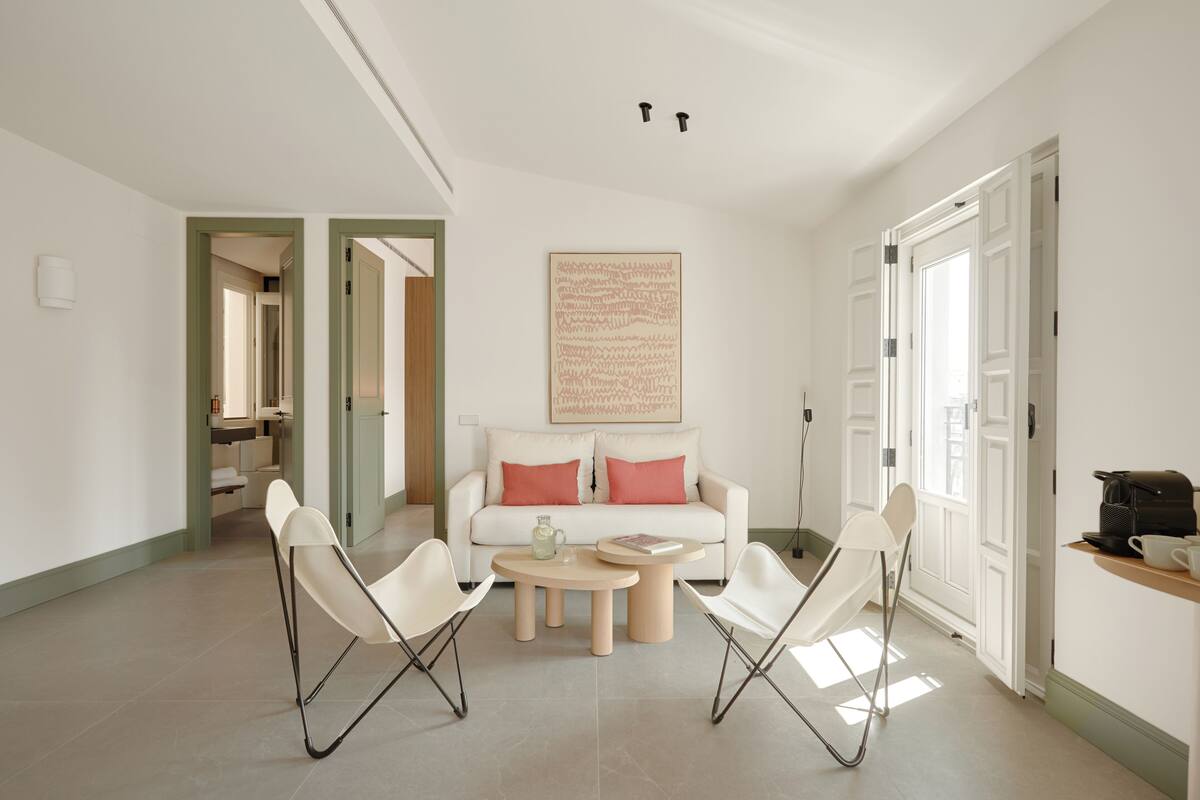 A modern living room with a white sofa, two white chairs, a small round table, and a large abstract painting on the wall.