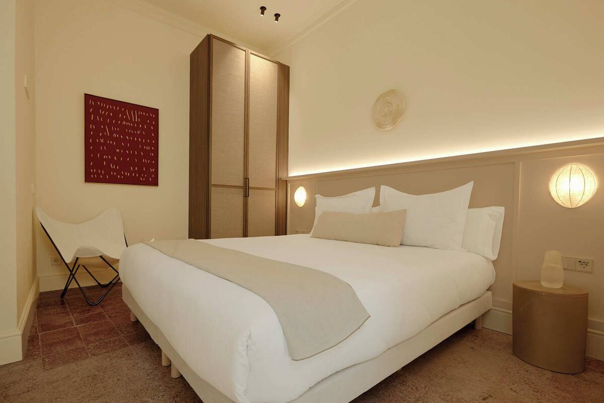 A hotel room with a large bed, a chair, a wardrobe, and a wall-mounted artwork.