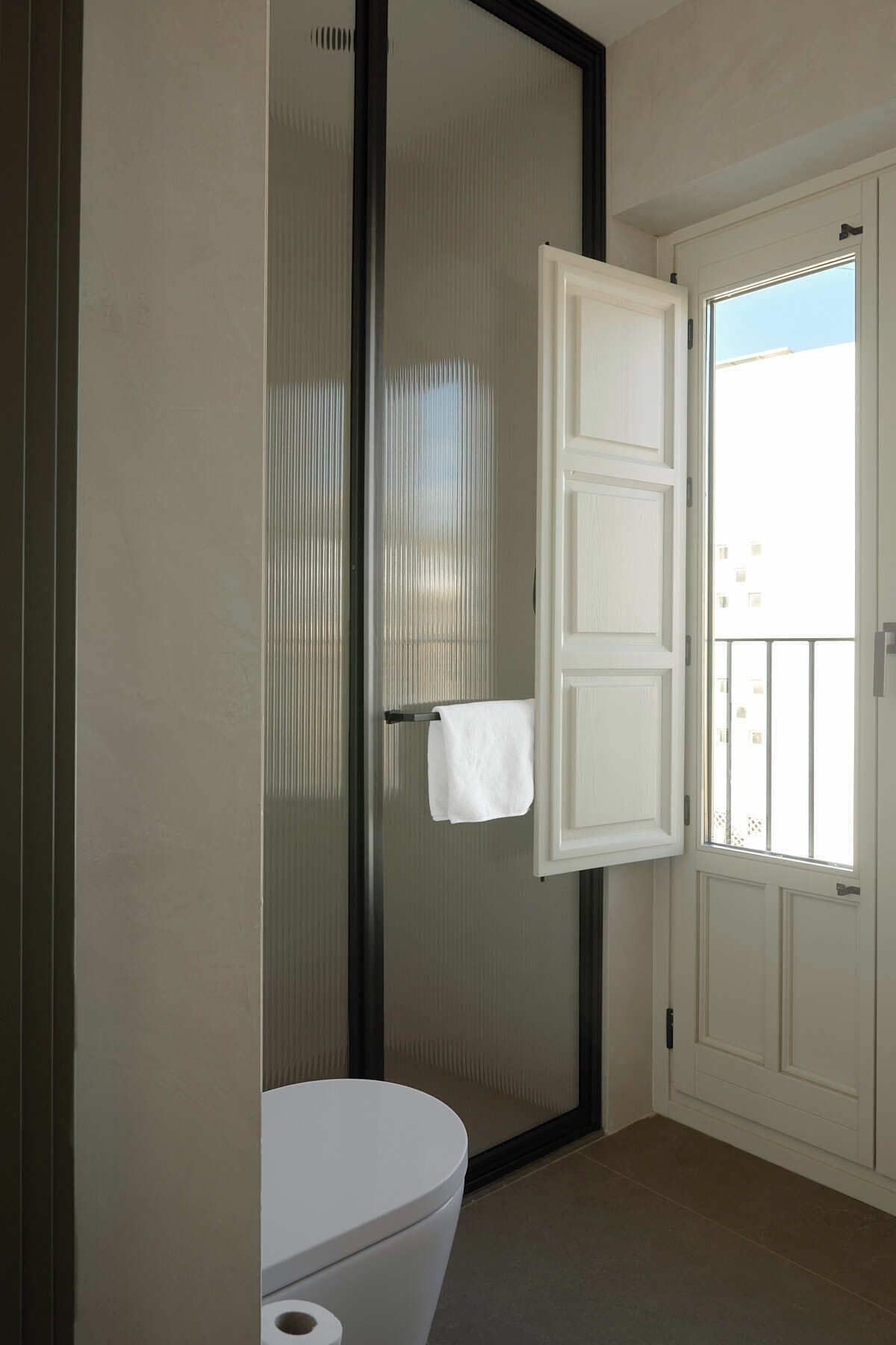 A bathroom with a toilet, a towel rack, and a door leading to a balcony.