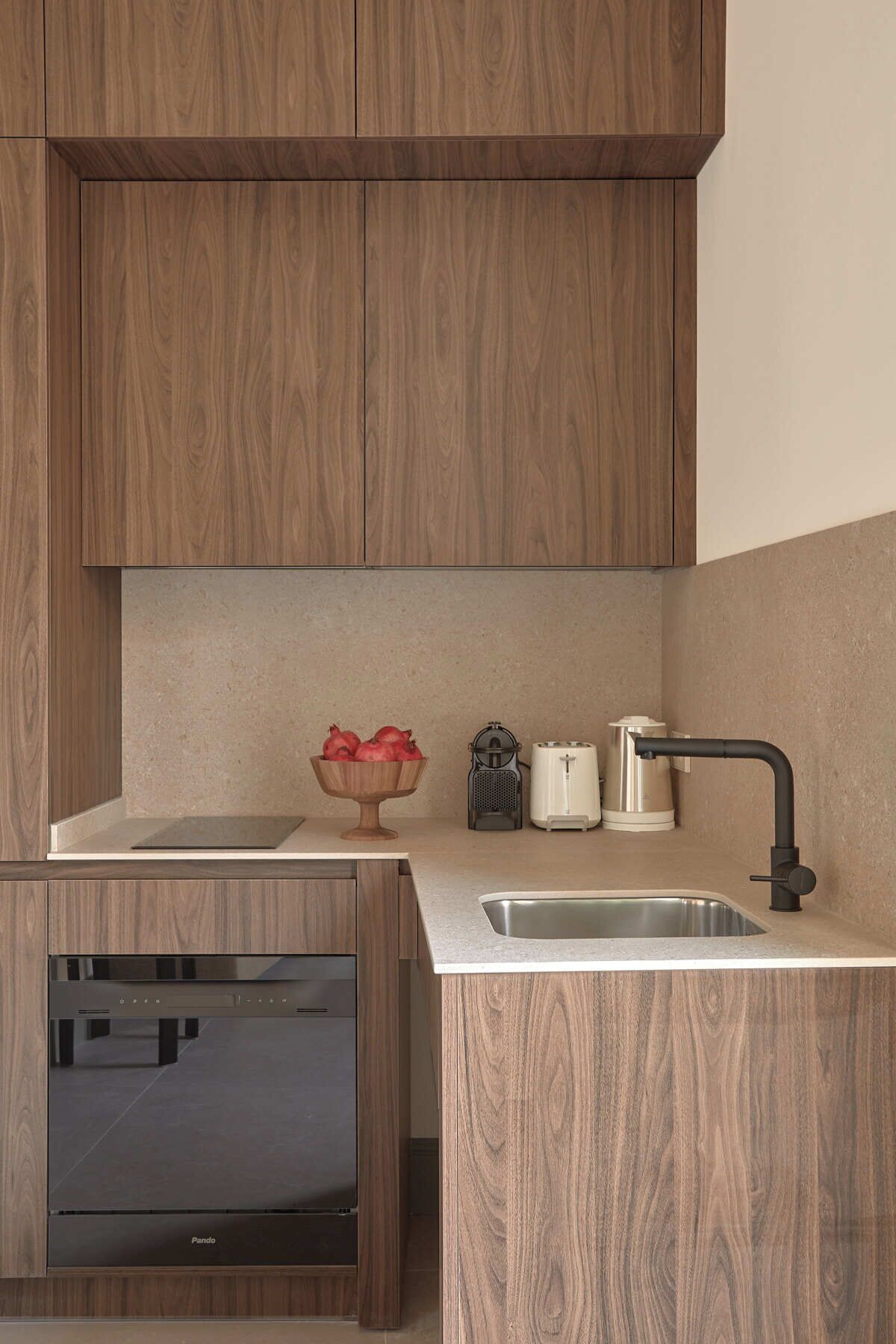 A modern kitchen with wooden cabinets, a built-in oven, a sink, and a countertop with a bowl of fruit and a coffee maker.