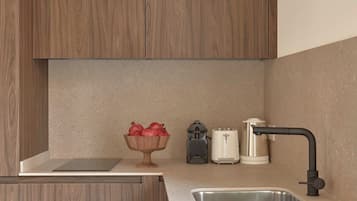 Una cocina moderna con armarios de madera, horno empotrado, pileta y una mesada con un cuenco de frutas y una cafetera.