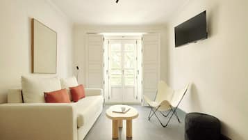 Un salon moderne avec un canapé, une petite table ronde, un fauteuil et un téléviseur à écran plat fixé au mur.