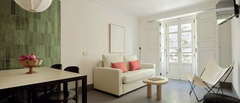 A modern living room with a dining area, a sofa, a coffee table, and a TV mounted on the wall.