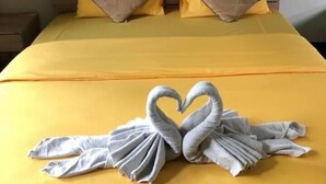 Ein Bett mit einer gelben Tagesdecke, zwei Kissen und ein Handtuch, das zu einem Herz geformt ist.