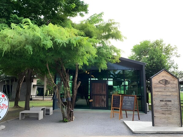 A modern building with a glass facade, wooden signage, and outdoor seating. - Smile buffalo resort (Manorom)