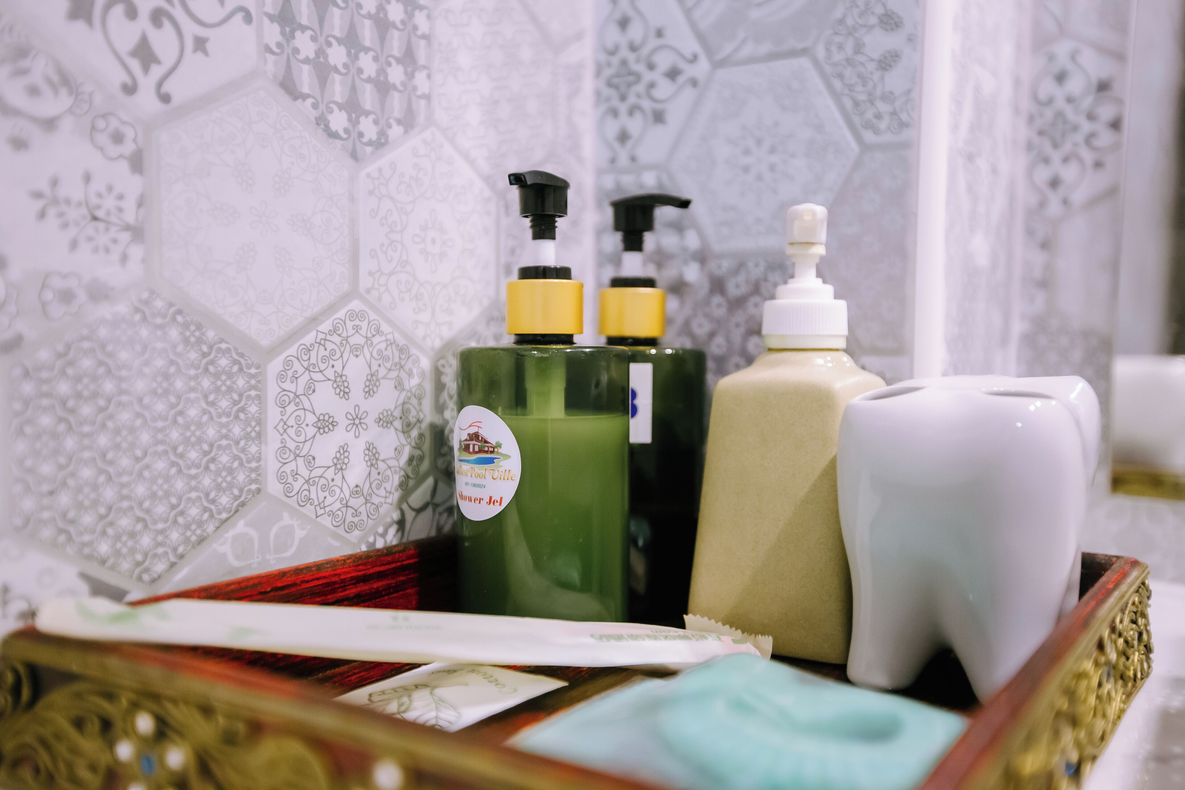 Un tocador de baño con un espejo decorativo, una botella verde de champú, una botella blanca de loción y un recipiente blanco para cepillos de dientes.