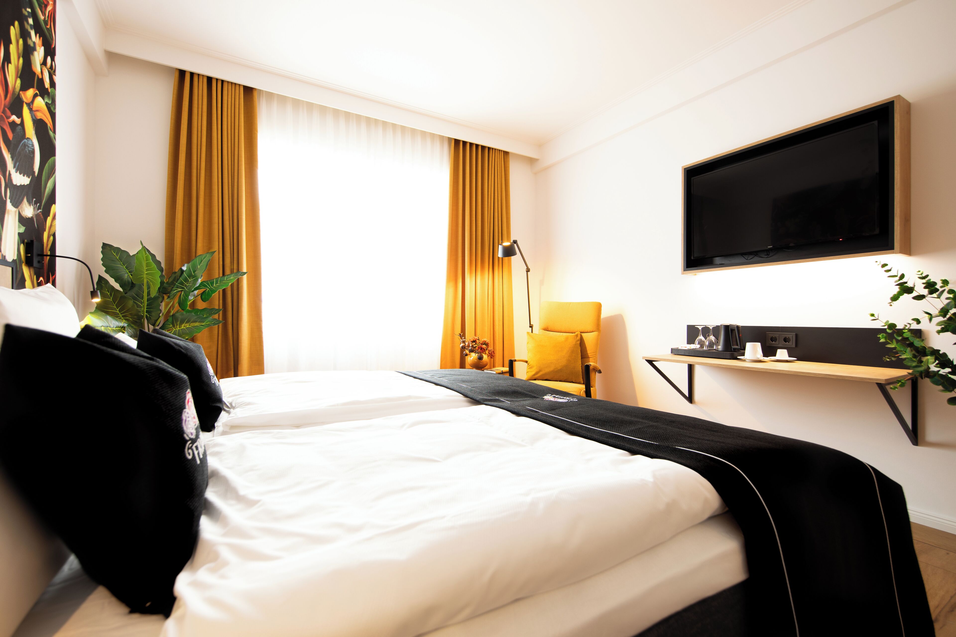 Ein Hotelzimmer mit Bett, Wandfernseher, Schreibtisch mit Lampe und einem Vorhangfenster.