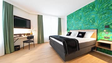 Et moderne hotelværelse med seng, skrivebord og et stort vindue med gardiner.