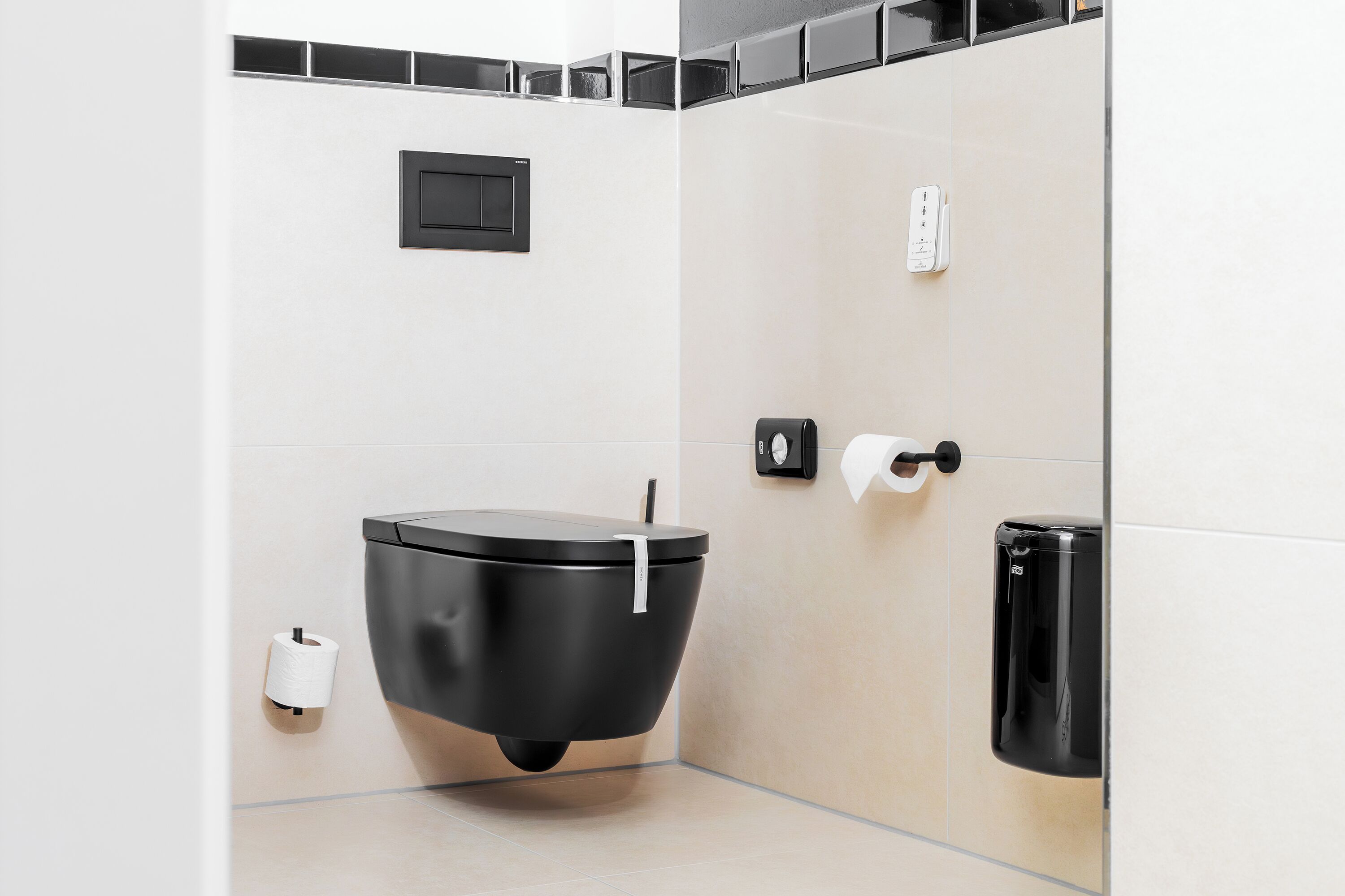 Une salle de bain moderne avec des toilettes noires, un distributeur d’essuie-tout et une poubelle.