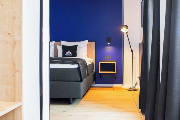 A bedroom with a bed, a bedside table, a lamp, and a wall-mounted light fixture. - Frida Hotel & Cafe (Bassum)