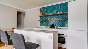 A modern kitchen with a central island, white cabinetry, and a teal backsplash. - SaintGermain Sojourn - Charming 2 bedroom in the Rive Gauche (Paris)