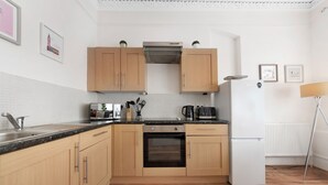 Una cocina moderna con armarios de madera, horno empotrado, refrigerador blanco y encimera negra.