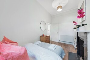 A bedroom with a bed, a dresser, a mirror, a radiator, and a fireplace. - Athenaeum Pl N10 | Muswell Hill | First Floor 1BD (London)