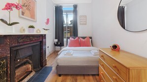 Un dormitorio con cama, cómoda, espejo, chimenea y ventana con cortinas.