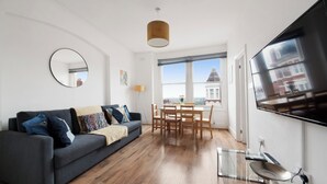 A modern living room with a grey sofa, wooden dining table, and a flat-screen TV mounted on the wall.