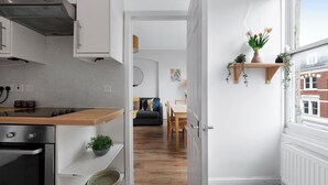A compact kitchen with modern appliances, a dining area with a wooden table and chairs, and a view of a red brick building through a window.