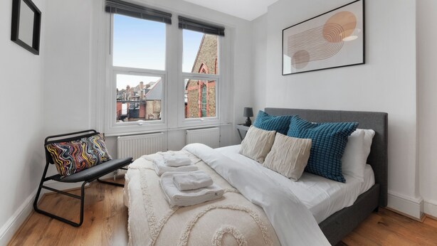 A bedroom with a bed, a chair, a window, and a framed artwork on the wall.