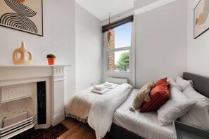 Ein Schlafzimmer mit Kamin, einem Bett mit weißer Bettwäsche und roten Kissen sowie einem Fenster mit Blick nach draußen.