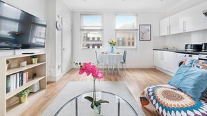 Ein modernes Apartment mit einem Flachbildfernseher, einem Essbereich mit Tisch und Stühlen, einer Küche mit Schränken und einem Sofa mit bunter Decke.