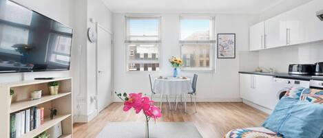 Een modern appartement met een flatscreen-tv, een eethoek met een tafel en stoelen, een keuken met kastjes en een bank met een kleurrijke deken.