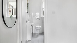 Ein schmaler Flur führt zu einem Badezimmer mit Toilette, Waschbecken und Spiegel.