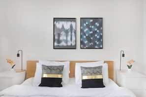 A neatly made bed with two pillows, a wooden headboard, and two bedside tables with lamps and potted plants.