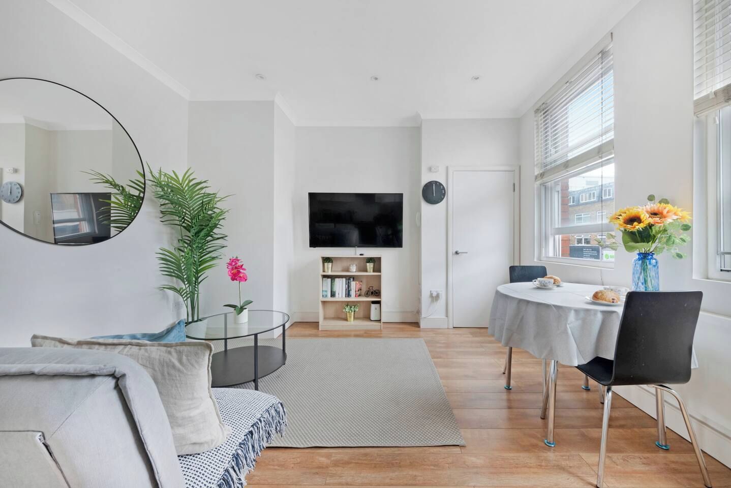 A modern living room with a sofa, a coffee table, a TV, a bookshelf, and a dining area with a table and chairs.