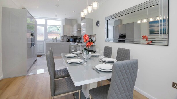 A modern kitchen with white cabinets, a dining table set for four, and a large mirror on the wall.