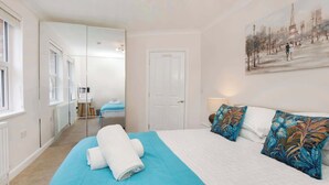 A bedroom with a bed, a blue blanket, a white door, and a painting on the wall.