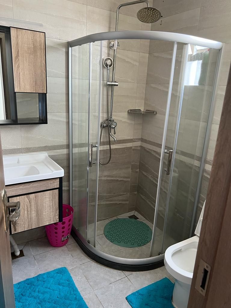 A modern bathroom with a glass-enclosed shower, a white sink, and a wooden vanity.