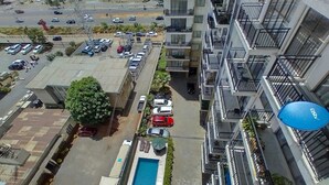 A high-rise building with multiple balconies, a swimming pool, and a parking lot with cars. - Lux Suites Vesta Gardens Apartments (Nairobi)