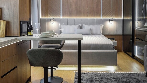 Quarto moderno e compacto com cama, mesas de cabeceira e um espaço de estar.